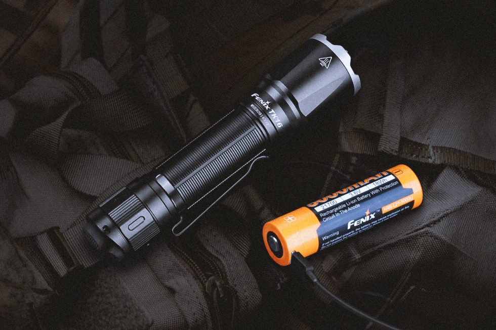Linterna táctica Fenix TK16 junto a una batería recargable conectada mediante cable USB.