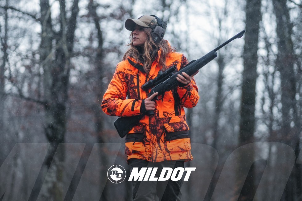 Cazadora con ropa naranja de alta visibilidad y rifle en un bosque nevado.