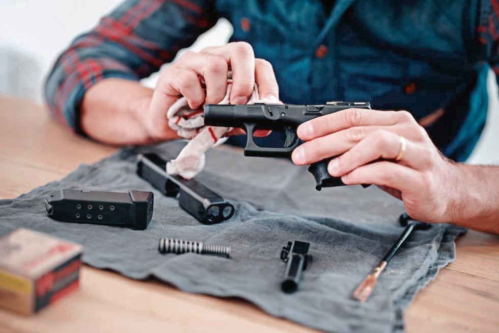 Persona limpiando una réplica de pistola de airsoft desmontada con un paño de mantenimiento, junto a sus componentes y herramientas de limpieza colocados sobre una superficie de trabajo